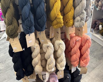 May include: A wall display of yarn skeins in various colors, including black, brown, beige, pink, red, yellow, blue, and gray. The yarn is arranged in rows and is labeled with the word "YARN" at the top.