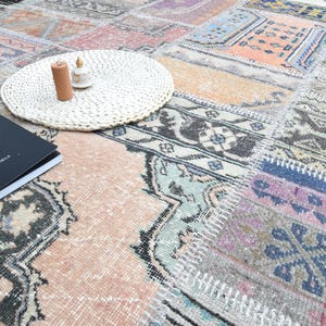 May include: A patchwork rug with a variety of colors and patterns, including pink, blue, and green. The rug is made of different pieces of fabric that have been sewn together. A book and a small white tray with two candles are on top of the rug.