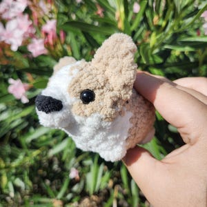 May include: A small, crocheted dog toy with brown and white fur. The toy has black eyes and a black nose.