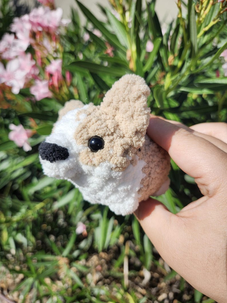 May include: A small, crocheted dog toy with brown and white fur. The toy has black eyes and a black nose.