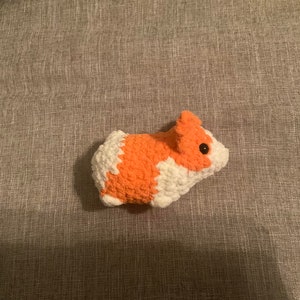 May include: A crocheted stuffed animal shaped like a guinea pig. The guinea pig is orange and white with a black eye.
