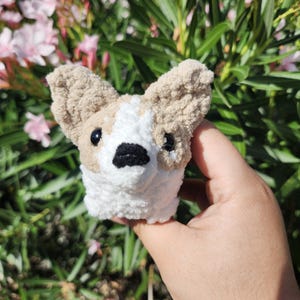 May include: A small crocheted dog toy with brown and white fur. The toy has black eyes and a black nose.