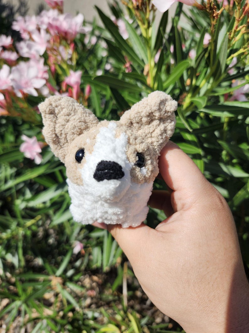 May include: A small crocheted dog toy with brown and white fur. The toy has black eyes and a black nose.