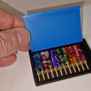 May include: A blue case with a black interior holds a set of 12 colorful, patterned, metal pen nibs with gold tips.