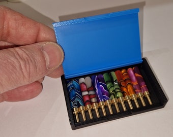 May include: A blue case with a black interior holds a set of 12 colorful, patterned, metal pen nibs with gold tips.