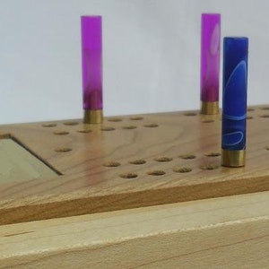 May include: A wooden game board with a grid of holes and pegs. There are four pegs in the holes, two purple and two blue.