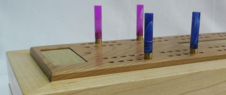 May include: A wooden game board with a grid of holes and pegs. There are four pegs in the holes, two purple and two blue.
