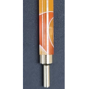 May include: A close-up of a small, orange and white patterned, cylindrical object with a gold metal tip. The object is on a dark gray background. The text "TT" is printed below the object.