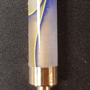 May include: A close-up of a white, blue, and yellow striped pen with a gold metal tip. The pen is on a black surface. SS