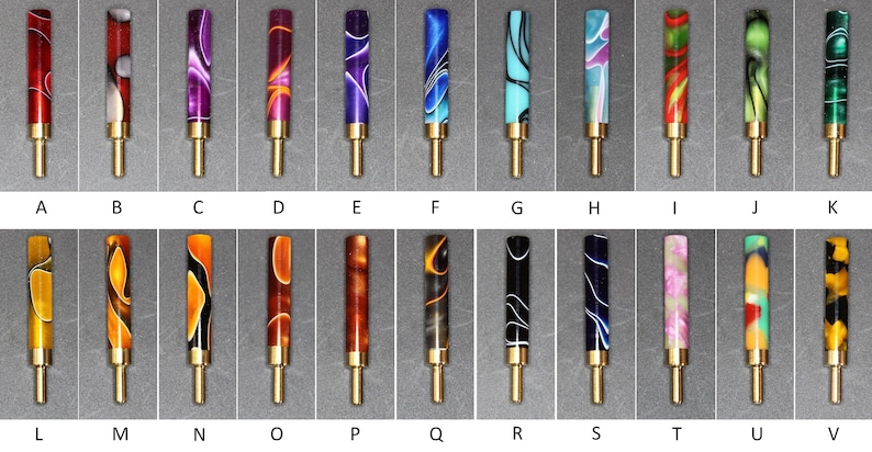 May include: Twenty-six different colored and patterned pen barrels with gold-colored metal tips and bases. The barrels are made of acrylic and have a variety of designs, including swirls, stripes, and geometric patterns.