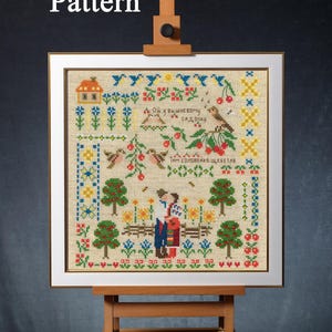 Könnte beinhalten: Gerahmtes Kreuzstichmuster mit einem Volkskunstdesign, das auf einer Holzstaffelei präsentiert wird. Die Stickerei zeigt eine farbenfrohe Szene mit Bäumen, Vögeln und Figuren, mit dem Text "PDF Pattern" oben.