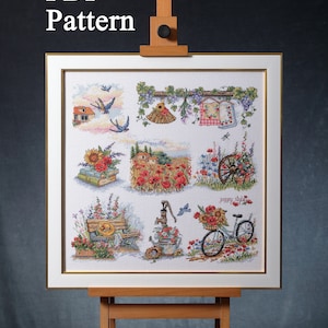 May include: A framed cross-stitch design with a rural theme, presented on a wooden easel. The artwork depicts several scenes, including houses, flowers, and a bicycle. The text "PDF Pattern" is visible at the top.