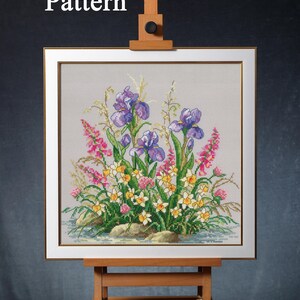 May include: A framed cross-stitch floral design featuring purple irises, pink flowers, and yellow and white daffodils. The artwork is displayed on a wooden easel. The words "PDF Pattern" are in the upper left corner.