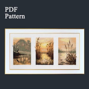May include: A framed cross-stitch landscape featuring three panels of a sunset over a lake. The panels depict reeds, a bridge, and a heron. The frame is white with a gold inner border. Text in the upper left corner reads "PDF Pattern."