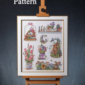 Puede incluir: Un patrón de punto de cruz enmarcado que presenta una variedad de diseños de temática primaveral, incluyendo flores, una casita para pájaros, un conejito y un pájaro. El patrón se muestra en un caballete.
