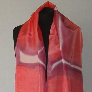 Op de afbeelding: Een lange, rode zijden sjaal met een wit en paars abstract ontwerp. De sjaal is dubbelgevouwen en gedrapeerd over de nek van een mannequin.