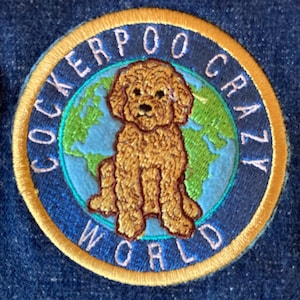 May include: A round, yellow embroidered patch with the words "Cockerpoo Crazy World" around a brown dog sitting on a blue and green globe.