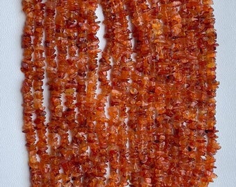 May include: A strand of carnelian chip beads, with a deep orange color and a natural, irregular shape. The beads are strung together in a long, continuous strand, and they have a slightly rough texture.