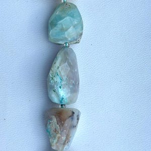 May include: A strand of five faceted gemstone beads, with a light blue, green, and white colour scheme. The beads are strung on a thin cord with a light blue tassel at the bottom.