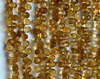 Könnte beinhalten: Eine Strähne aus facettierten, tropfenförmigen, goldbraunen Edelsteinperlen. Die Perlen sind auf einem dünnen Draht aufgefädelt und haben einen Durchmesser von etwa 8 mm.