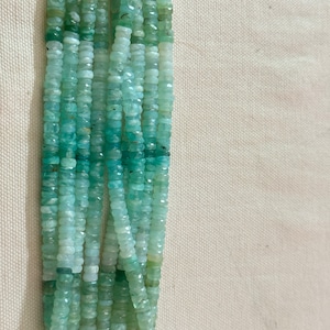 May include: A strand of light green gemstone beads. The beads are faceted and have a slightly irregular shape. The beads are strung on a clear thread.