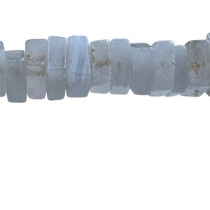 Puede incluir: Un collar de cuentas rectangulares de color azul claro. Las cuentas tienen una forma ligeramente irregular y una calidad translúcida. Las cuentas están ensartadas, creando un collar o pulsera.