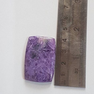 May include: A purple and white cabochon gemstone measuring approximately 2.5 cm in length. The stone has a unique, swirling pattern.