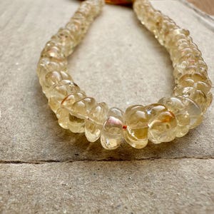 May include: A long strand of light yellow gemstone beads, each bead is faceted and has a slightly irregular shape. The beads are strung on a thin, clear thread.