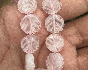 May include: A strand of pink rose quartz beads, each carved with a leaf design. The beads are strung on a cord with a pink tassel.