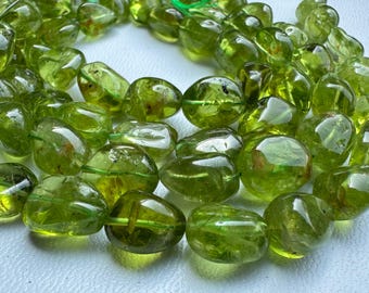 Puede incluir: Un hilo de cuentas de peridoto pulidas y translúcidas en un tono verde lima vibrante. Las cuentas tienen formas irregulares, son lisas y redondeadas, presentan inclusiones naturales y un acabado brillante, ensartadas en un cordón fino.