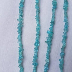 May include: A strand of light blue aquamarine chip beads. The beads are small and irregular in shape, and they are strung on a clear thread.