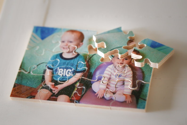 May include: A wooden jigsaw puzzle with two children on it. The puzzle is partially assembled. The boy is wearing a blue shirt with the word "BIG" on it. The girl is wearing a striped shirt.
