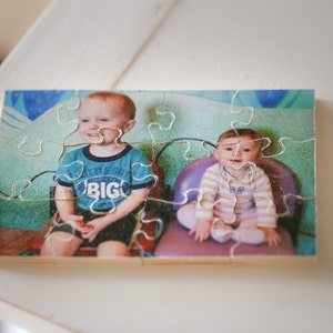 May include: A wooden jigsaw puzzle with a photo of two children. The boy is wearing a blue shirt with the words "Little Guy Big" on it. The girl is wearing a striped shirt and sitting in a purple chair.