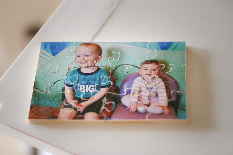 May include: A wooden jigsaw puzzle with a photo of two children. The boy is wearing a blue shirt with the words "Little Guy Big" on it. The girl is wearing a striped shirt and sitting in a purple chair.