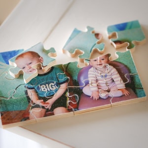 May include: A wooden jigsaw puzzle with a photo of two children. The child on the left is wearing a blue shirt with the words "Little Boy Big" printed on it. The child on the right is wearing a striped shirt. The puzzle is partially assembled.