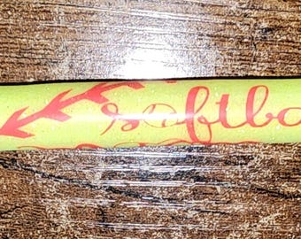 May include: A yellow pen with the word "Softball" in red script and red stitching-like designs. The pen has a black tip and a silver metal end.