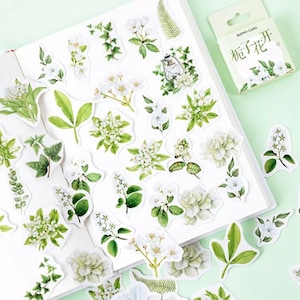Peut inclure: Une feuille d'autocollants blancs avec des illustrations de feuilles vertes et de fleurs blanches. Les autocollants sont dans une petite boîte avec le texte "Memo-Card  栀子花" sur le devant.