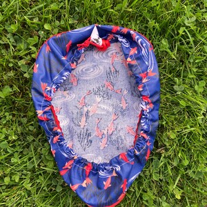 May include: A blue and red fabric cover with a white drawstring. The fabric has a pattern of red fish swimming in blue water with white waves.