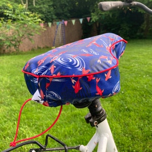 May include: A blue bicycle seat cover with a red trim and a pattern of red fish swimming in blue water. The cover has a red drawstring.