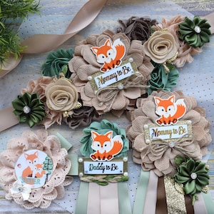 May include: Three brown and green floral sashes with a fox design and the text "Mommy to Be" and "Daddy to Be". The sashes are decorated with faux flowers, leaves, and a small fox figurine.