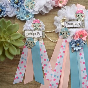 May include: Two blue and pink sashes with white polka dots and a white, blue, and pink flower embellishment. Each sash has a small elephant with a hat and a sign that says "Mommy to Be" and "Daddy to Be".