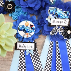 May include: Two blue and white checked sashes with blue and white rosettes. The rosettes have a racing car design and the sashes say "Mommy to Be" and "Daddy to Be".