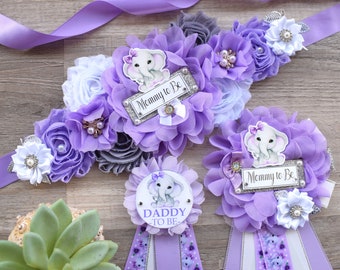 May include: Purple, white, and gray flower sashes with a baby elephant design and the text "Mommy to Be" and "Daddy to Be".