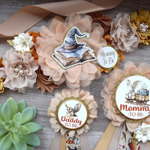 May include: A collection of floral baby shower decorations, including a sash with fabric flowers and a "Mommy To Be" badge. The sash features a wizard hat and book graphic. Additional badges say "Daddy To Be".