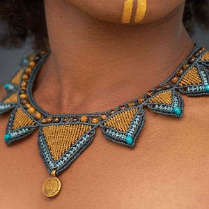 Op de afbeelding: Een bruine en grijze kralenketting met een gouden munt hanger. De ketting heeft een geometrisch patroon met turquoise kralen.