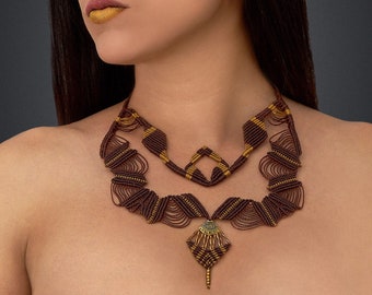 Puede incluir: Una mujer con maquillaje dorado en la cara lleva un collar de capas marrón y dorado con un colgante. El collar está hecho de cordón trenzado y tiene un diseño geométrico.