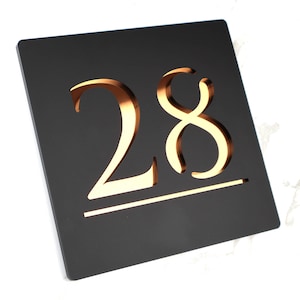 May include: Black square house number sign with gold-colored numerals "28" on a black background.