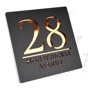 May include: Black square house number sign with gold raised numbers 28 and the text "Honeysuckle Avenue" underneath.
