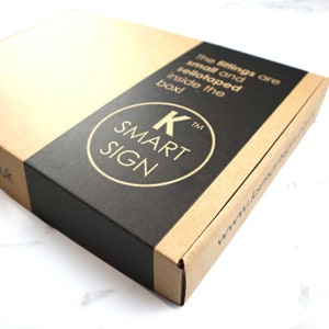 May include: A brown cardboard box with a black label that says "K SMART SIGN" in gold lettering. The text on the box says "The fittings are small and sellotaped inside the box!"