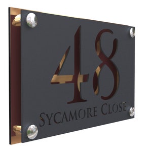 Puede incluir: Un letrero de número de casa de metal negro con el número 48 recortado y las palabras "SYCAMORE CLOSE" debajo. El letrero tiene tornillos plateados y un borde dorado.